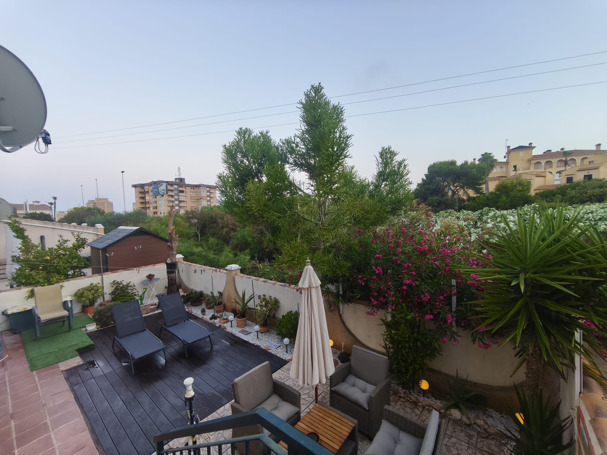 Elevated view of terrace with sun loungers, rattan furniture, closed parasol, flowering oleander, and neighborhood views