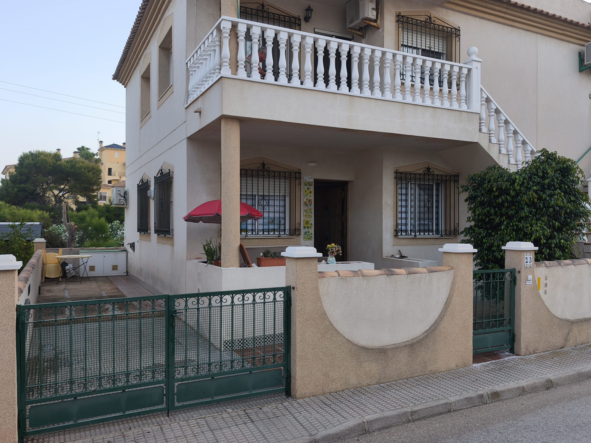 Building exterior with covered entrance porch, wrought-iron window grilles, white balustrade upper balcony, and green gate